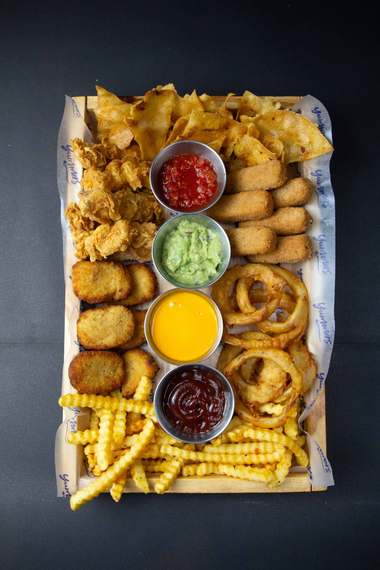 Tabla para compartir de Yummers — nuggets, alitas, aros de cebolla, papas y salsas, fotografía cenital